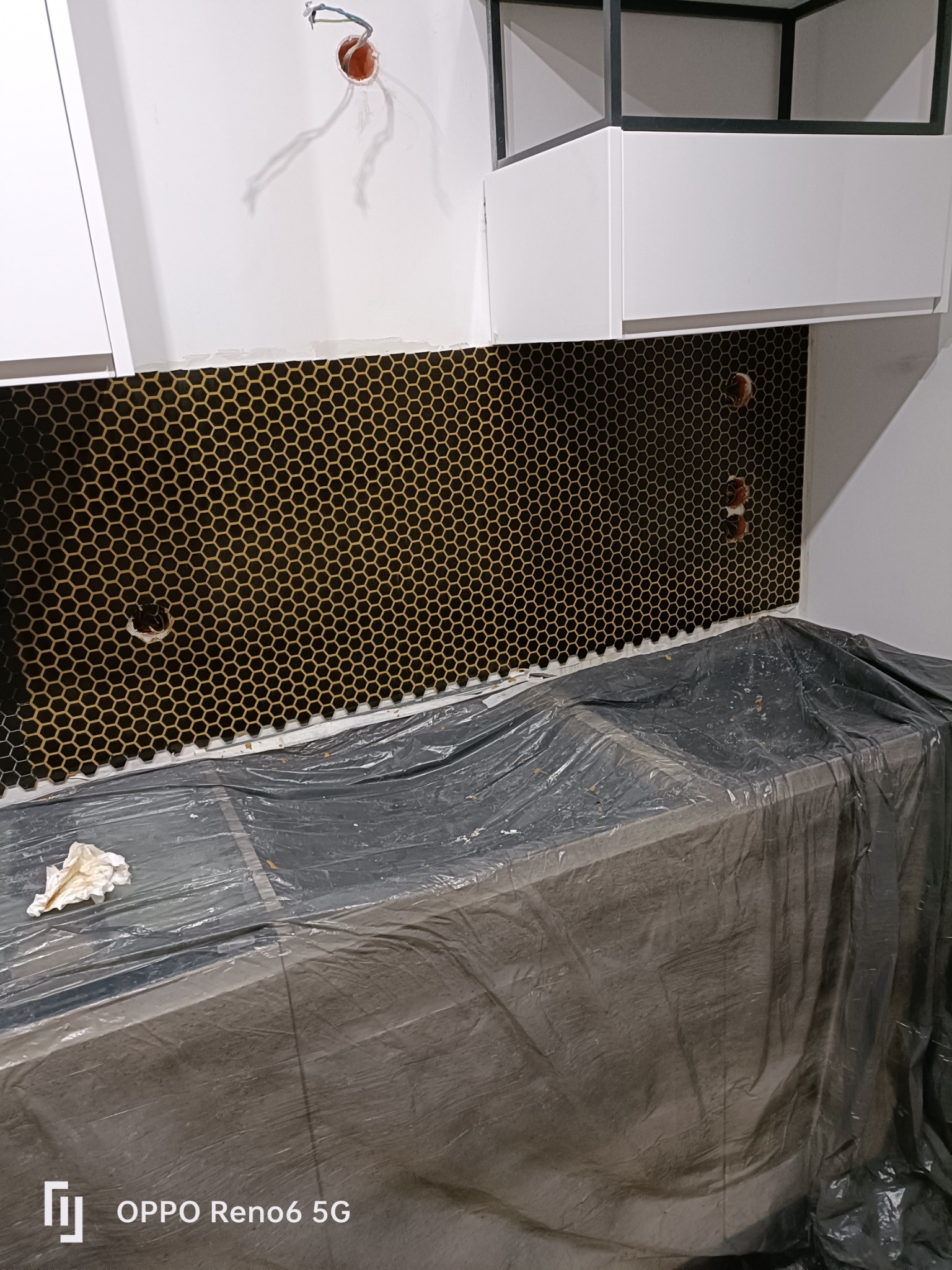 Ściana w kuchni z ułożoną mozaiką heksagonalną w kolorze czarnym i złotym, zabezpieczony blat roboczy folią malarską, widoczne puszki elektryczne bez osprzętu.