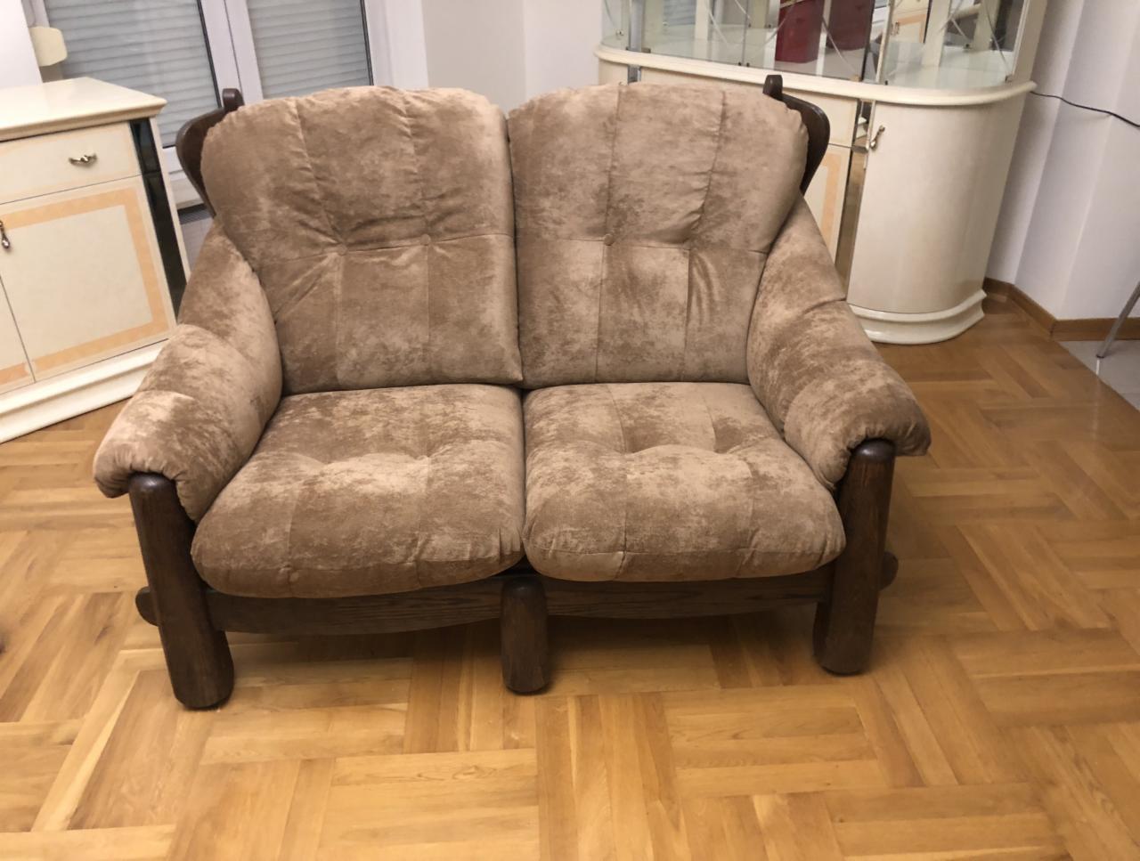 Dwuosobowa sofa z brązową tapicerką z mikrofibry, z drewnianymi ramami i nogami, ustawiona na parkiecie.