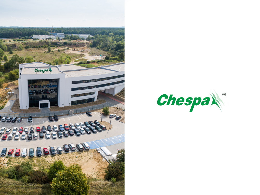 Zdjęcie z lotu ptaka przedstawiające nowoczesny budynek biurowy z logo Chespa i parkingiem pełnym samochodów, z terenami zielonymi i żwirownią w tle.