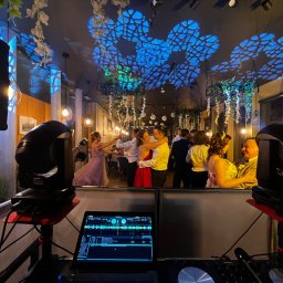 Marian Nowak - Parkiet taneczny z bawiącymi się ludźmi, oświetlony dekoracyjnymi światłami i nagłośniony sprzętem DJ-skim. Widoczne reflektory i laptop z programem muzycznym.