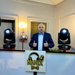Marian Nowak - DJ w niebieskiej muszce za konsoletą z logo 'MANIX', oświetlony reflektorami. Uśmiechnięty mężczyzna z uniesionymi kciukami, gotowy do występu na imprezie.