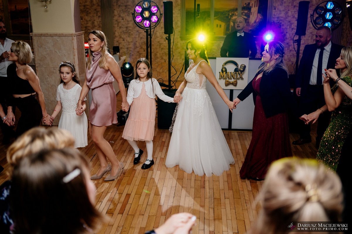 Wspólny taniec na parkiecie weselnym, oświetlonym kolorowymi światłami. W tle DJ za konsoletą z logo 'MANIX'.