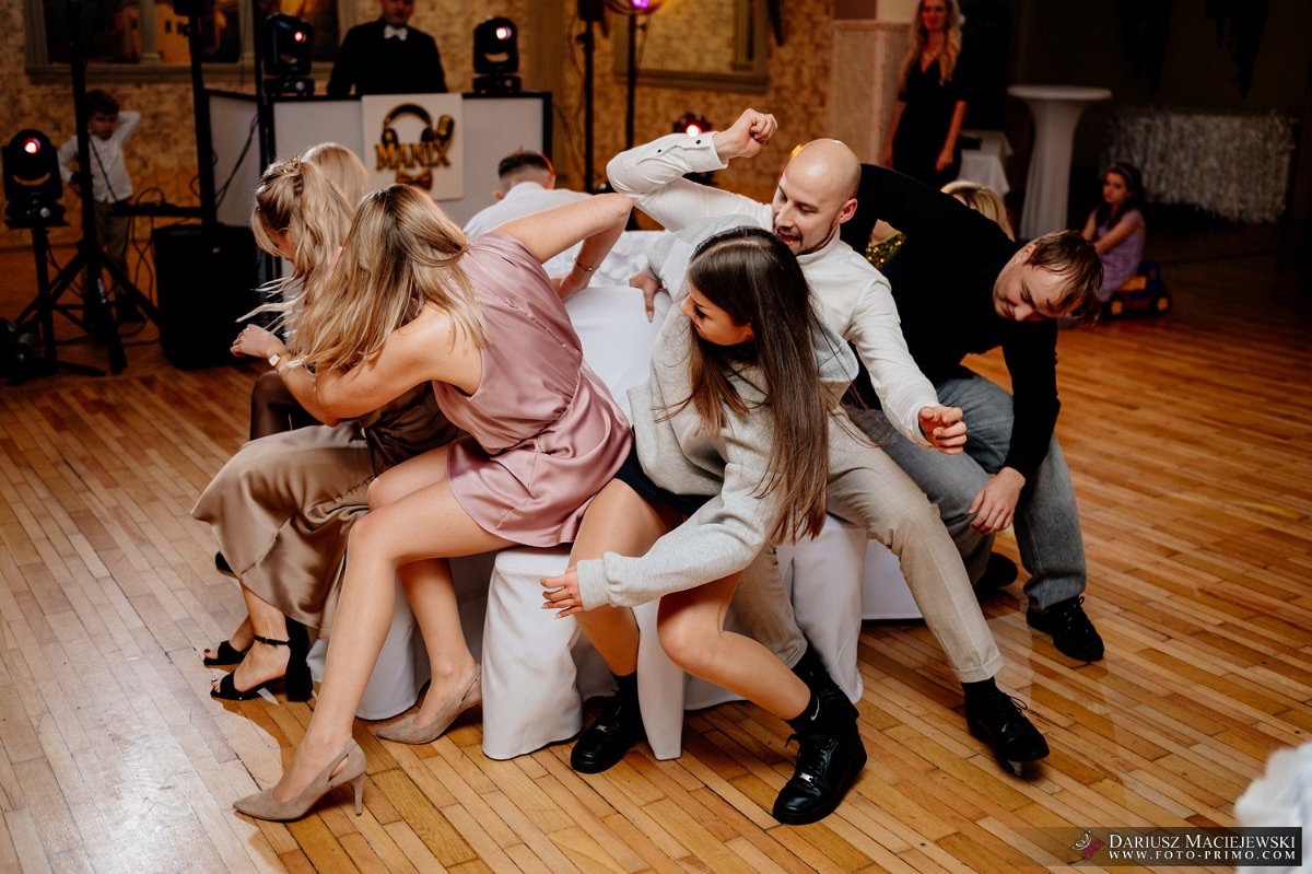 Zabawa gości podczas oczepin na weselu. W tle DJ z oświetleniem. Parkiet z jasnego drewna. Dynamiczne ujęcie z bliska, uchwycone emocje i ruch.