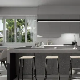 Nowoczesna kuchnia z szarymi szafkami, wyspą z blatem z szarego kamienia i trzema wysokimi stołkami barowymi z jasnego drewna na czarnych nogach. W tle duże okno z widokiem na zieleń.