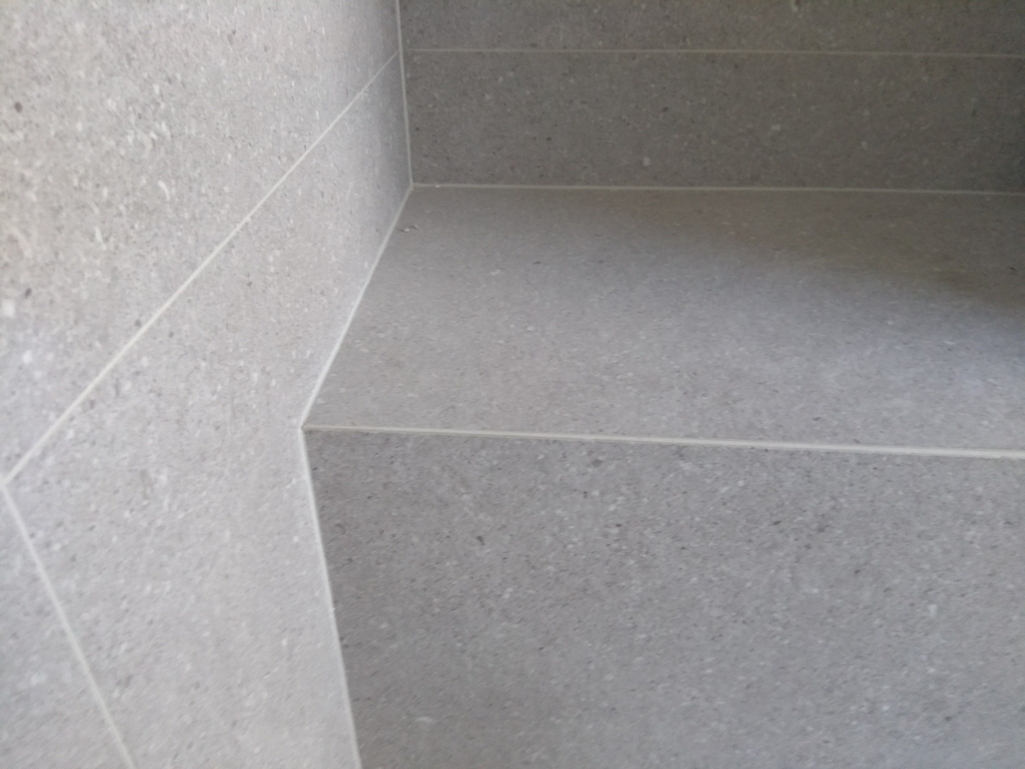 Szczegółowe ujęcie szarej, ceramicznej zabudowy brodzika, z precyzyjnie ułożonymi płytkami i fugami, wykonane przez firmę z Elbląga.