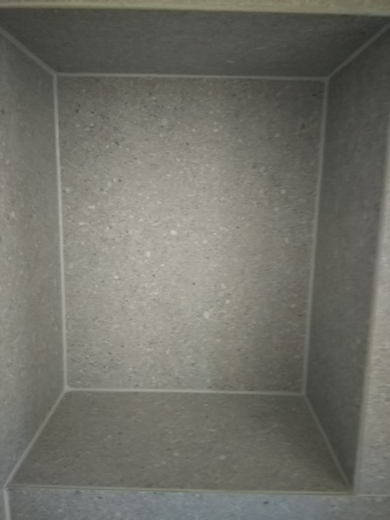 Wnęka wyłożona szarą, nakrapianą płytką ceramiczną, wykończona białym silikonem, w trakcie prac wykończeniowych.