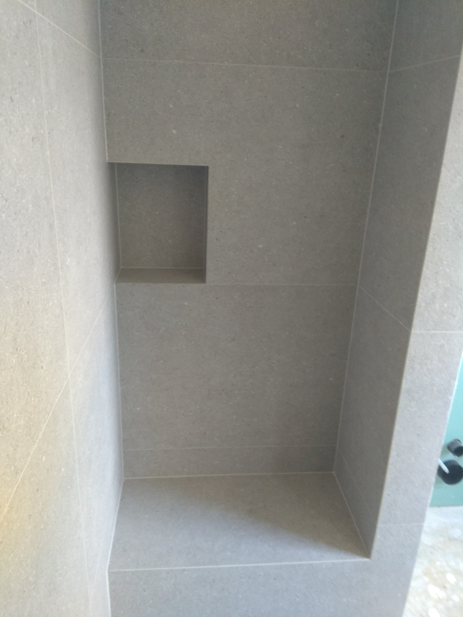 Wykończona wnęka prysznicowa z szarych, matowych płytek, widoczne fugi i narożnik ściany. Minimalistyczny design.