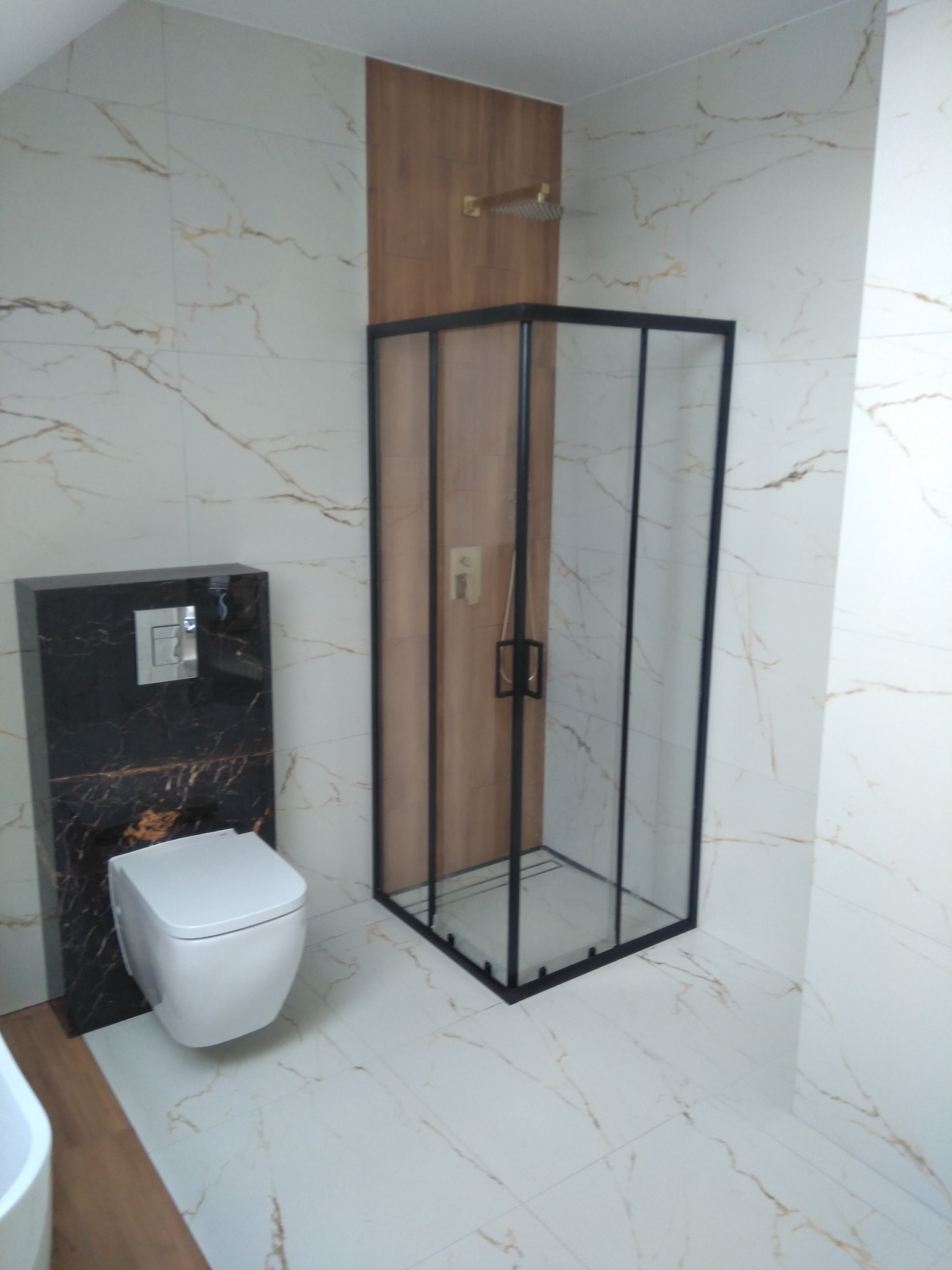 Nowoczesna łazienka z kabiną prysznicową z czarną ramą, podwieszaną toaletą w obudowie z czarnego marmuru i płytkami imitującymi marmur z delikatnym, złotym żyłowaniem na ścianach i podłodze.