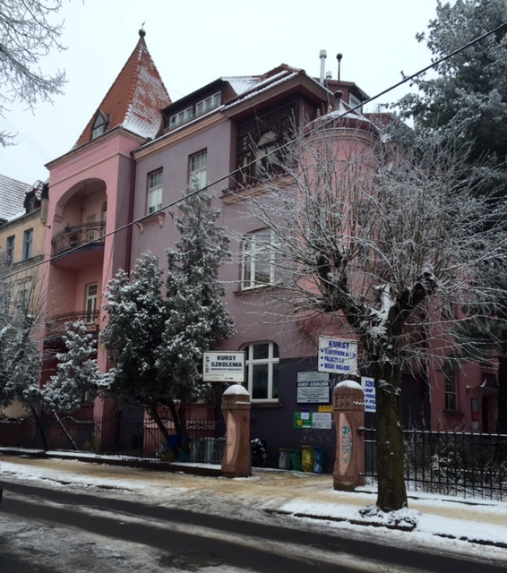 Budynek szkoły kursów i szkoleń w zimowej scenerii, tablice informacyjne przy wejściu.