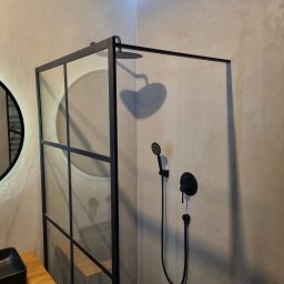 ALFA-BUD KM SPÓŁKA Z OGRANICZONĄ ODPOWIEDZIALNOŚCIĄ - Nowoczesna kabina prysznicowa z czarną ramą i armaturą na ścianie o fakturze betonu, widoczna umywalka nablatowa i okrągłe lustro.