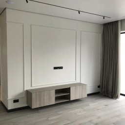 ALFA-BUD KM SPÓŁKA Z OGRANICZONĄ ODPOWIEDZIALNOŚCIĄ - Nowoczesne wykończenie wnętrza w Warszawie: minimalistyczna ściana z dekoracyjnymi panelami, podwieszana szafka RTV z drewnopodobnym fornirem i parkiet ułożony w jodełkę.