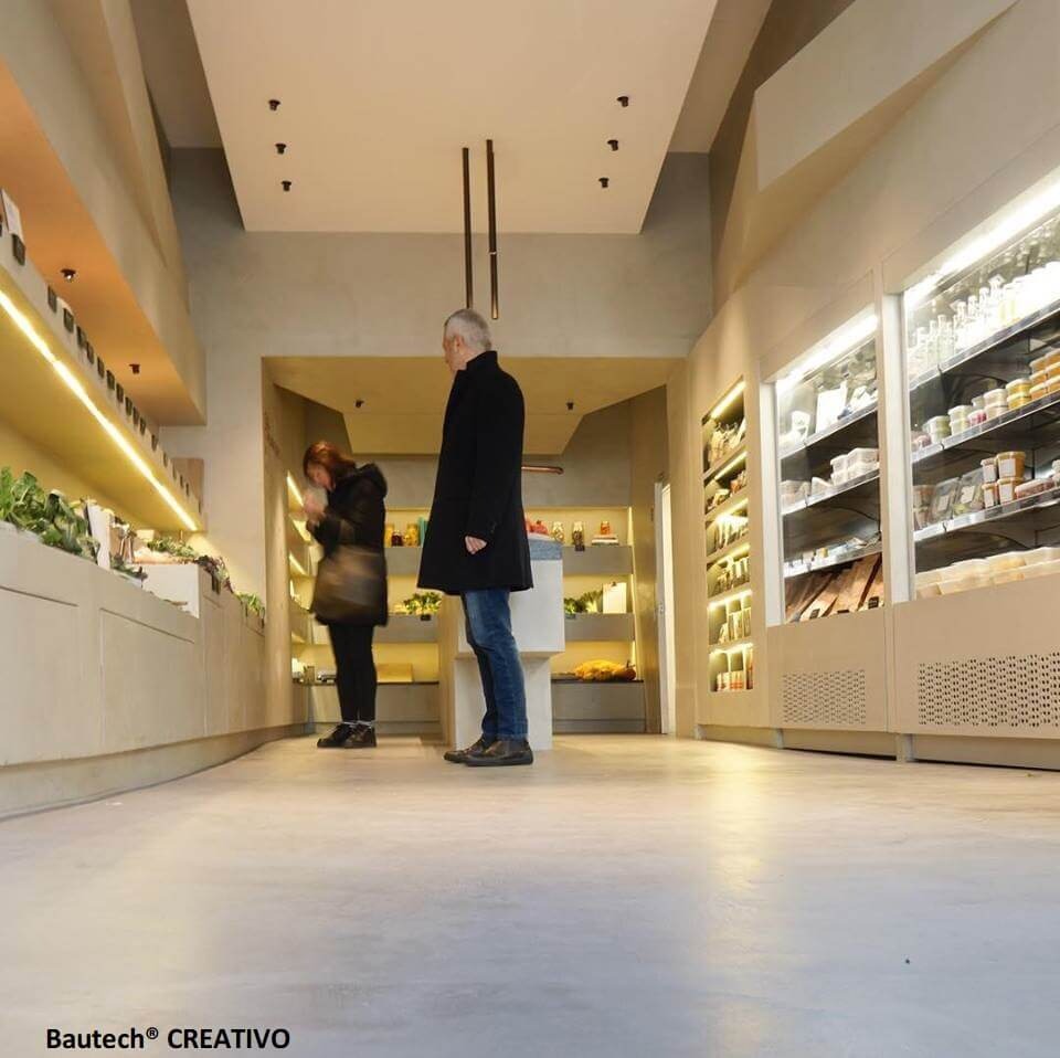 Jasnoszara posadzka w sklepie spożywczym z oświetleniem punktowym i klientami oglądającymi produkty.