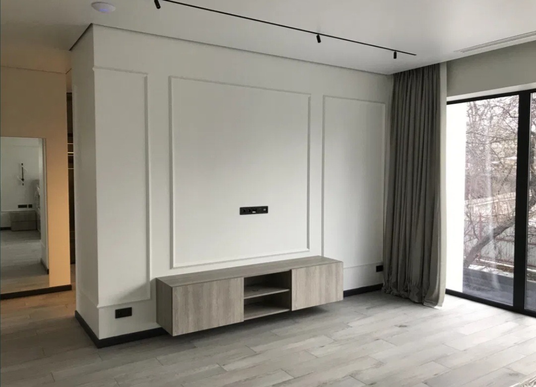 Nowoczesne wykończenie wnętrza w Warszawie: minimalistyczna ściana z dekoracyjnymi panelami, podwieszana szafka RTV z drewnopodobnym fornirem i parkiet ułożony w jodełkę.