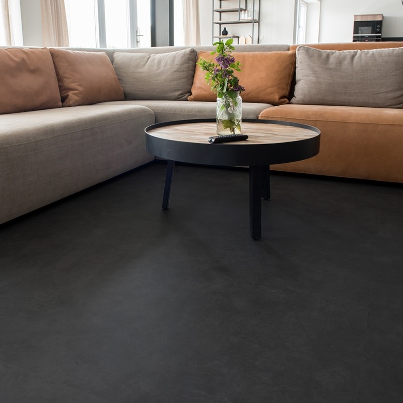 Ciemnoszara, jednolita posadzka w salonie z narożnikiem i stolikiem kawowym z bukietem kwiatów w wazonie.