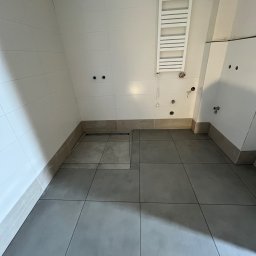 Eagle Eye - Wykończona łazienka z szarymi płytkami podłogowymi i białymi płytkami ściennymi. Widoczny grzejnik drabinkowy i przygotowane punkty instalacyjne.