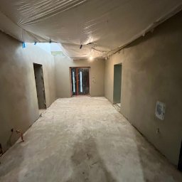 Eagle Eye - Pokój w trakcie prac wykończeniowych: świeżo nałożone gładzie na ścianach, podłoga przygotowana, sufit zabezpieczony folią malarską. Widoczne drzwi i otwory drzwiowe.