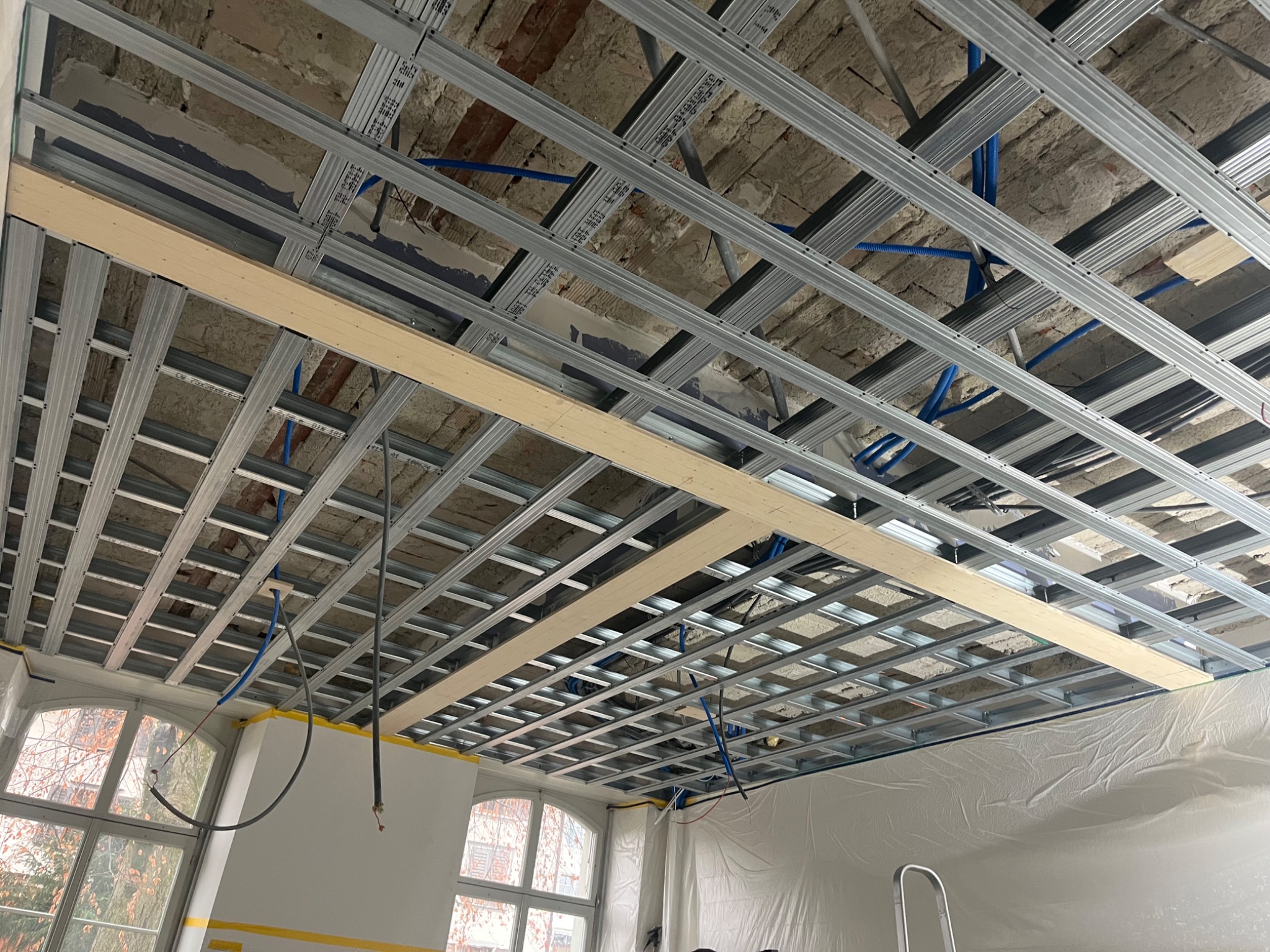 Montaż metalowej konstrukcji sufitu podwieszanego z płyt karton-gips, widoczne profile i instalacje. Przygotowanie do wykończenia wnętrza, surowy stan.