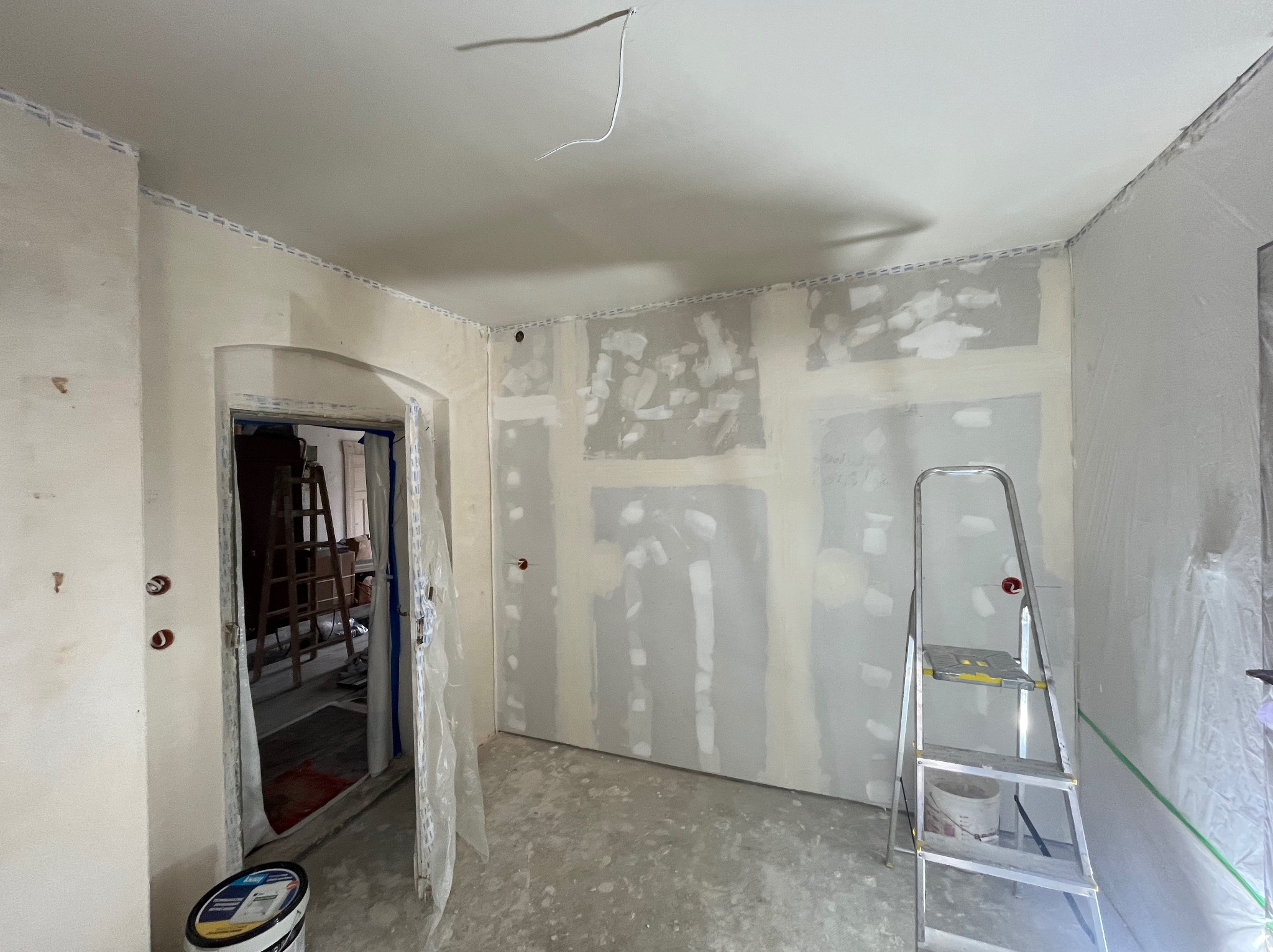 Pokój w trakcie remontu: ściany z płyt gipsowo-kartonowych, częściowo zaszpachlowane, drabina malarska, wiadro z farbą. Widoczne przygotowania do malowania.