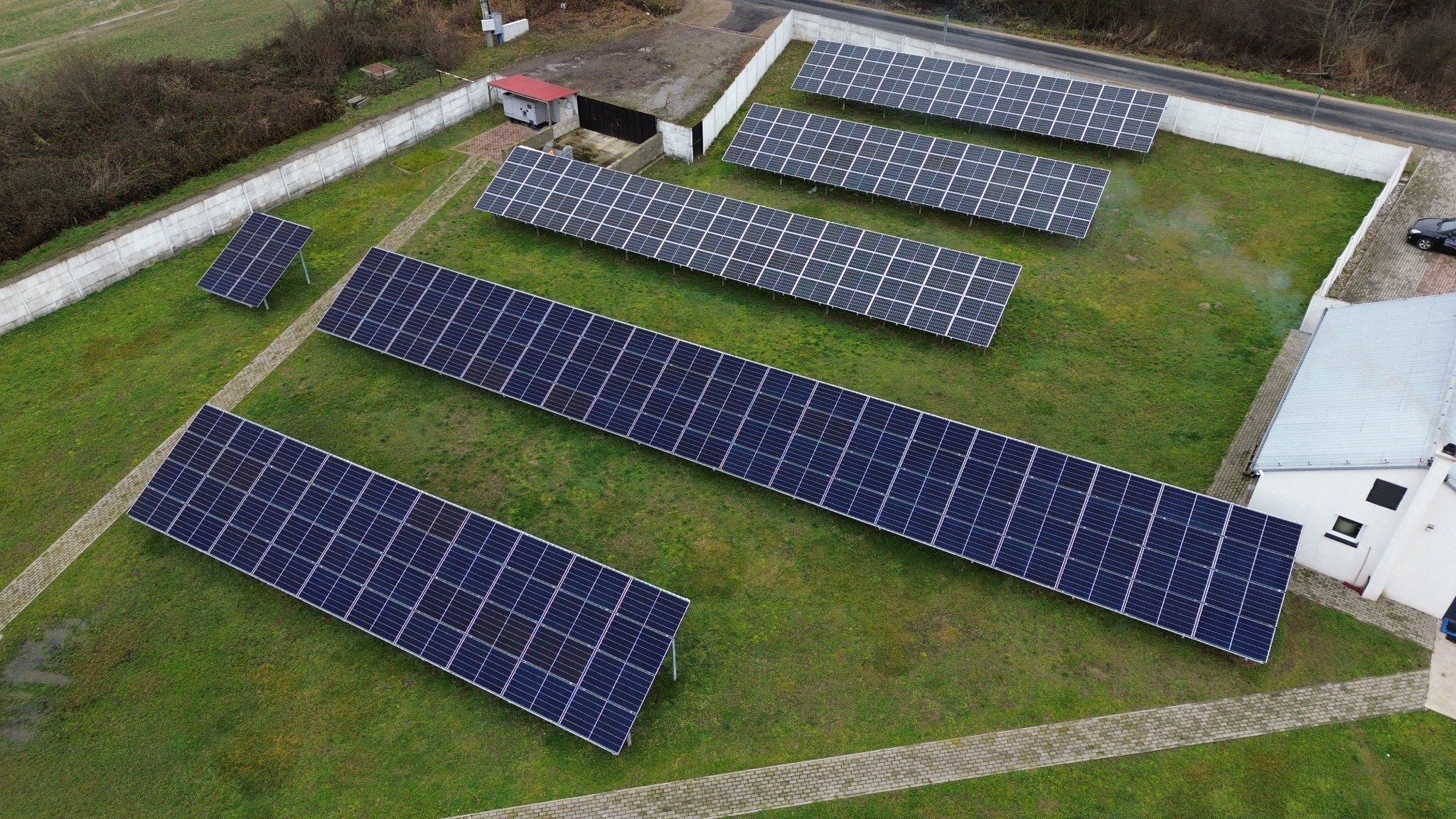 Widok z góry na instalację paneli słonecznych w Brzegu, rozmieszczonych na zielonej trawie obok budynków.