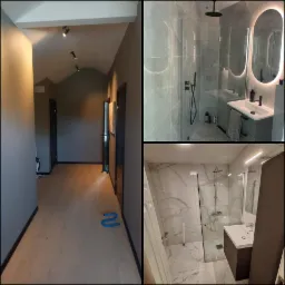 Nowoczesne łazienki z kabinami prysznicowymi typu walk-in, wykończone w szarościach i bieli, widoczne z perspektywy korytarza z oświetleniem punktowym.