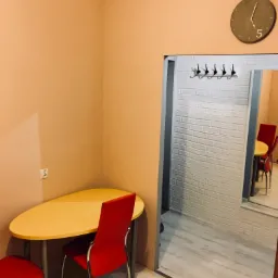 Wnętrze po odświeżeniu: żółty stół i czerwone krzesła w pokoju z pomarańczowymi ścianami, widok na przedpokój z białą cegłą i wieszakami na ubrania, zegar na ścianie.