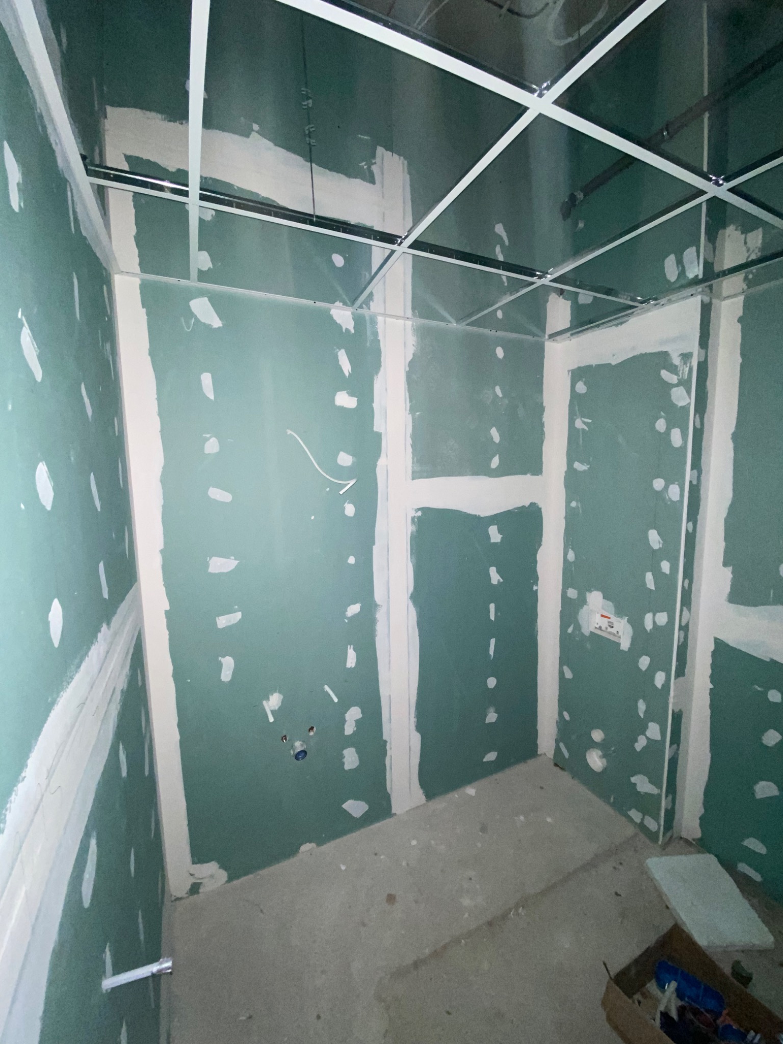 Wnętrze w trakcie montażu płyt kartonowo-gipsowych: widoczne metalowe profile sufitowe, ściany z płyt G-K z widocznymi punktami szpachlowania, instalacja elektryczna i hydrauliczna w ścianie...