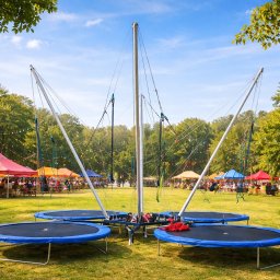 Nadmuchani - Cztery okrągłe trampoliny bungee na zielonej trawie, w tle kolorowe namioty i drzewa, tworzące plenerową strefę rozrywki.