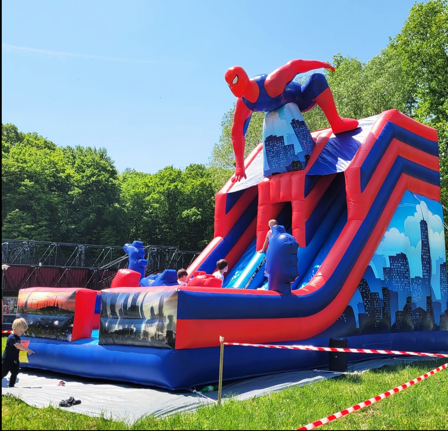 Kolorowa konstrukcja rekreacyjna ze Spidermanem w Wodzisławiu Śląskim. Dzieci bawią się na tle zieleni i błękitnego nieba. Atrakcja na imprezę plenerową.