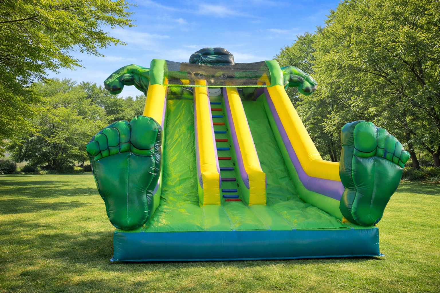 Kolorowa, dmuchana zjeżdżalnia w kształcie Hulka na trawie, z zielonymi rękami i stopami. Idealna atrakcja na imprezy plenerowe dla dzieci.