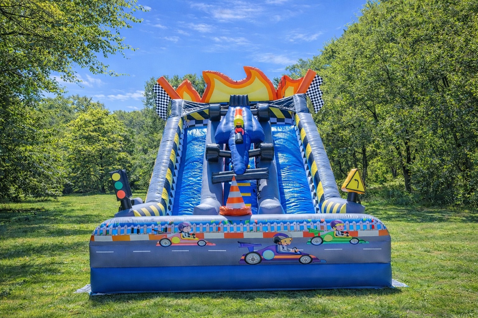 Kolorowa, dmuchana zjeżdżalnia w motywie wyścigów samochodowych na trawie, z drzewami w tle. Zjeżdżalnia ma kształt toru wyścigowego z dekoracjami i grafikami aut.