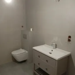 Szara łazienka w Bielsku-Białej z podwieszaną toaletą i szafką pod umywalkę z szufladami, widoczne niedokończone podłączenie elektryczne.