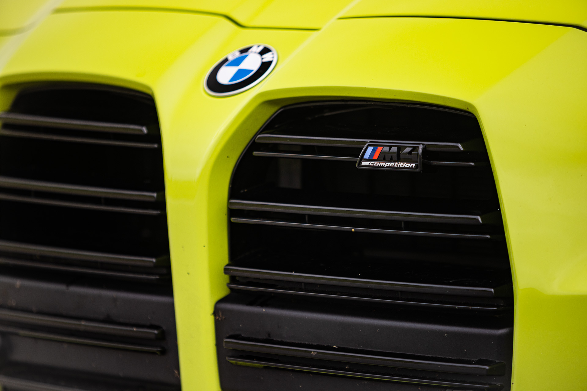 Żółty BMW M4 Competition z widoczną atrapą chłodnicy i logo BMW, detale lekko zabrudzone.