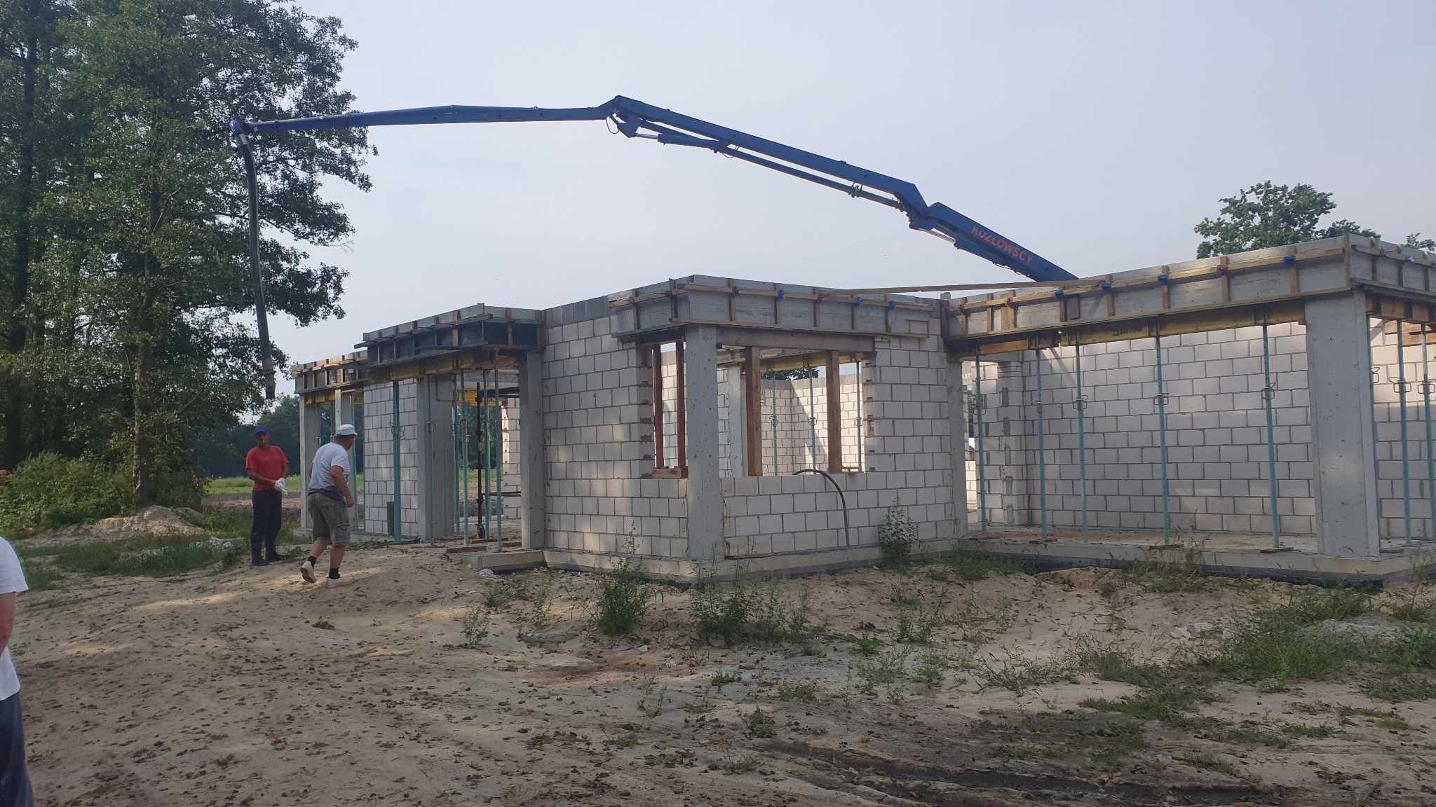 Budowa domu z betonu komórkowego, widoczny żuraw podający beton, pracownicy w pobliżu
