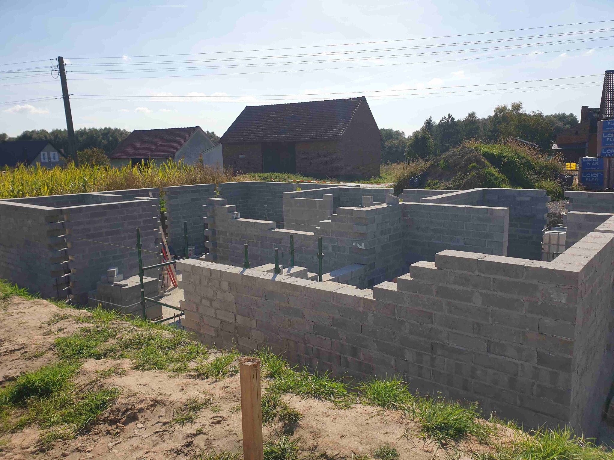 Wznoszone ściany fundamentowe z bloczków betonowych na tle wiejskich zabudowań i błękitnego nieba.