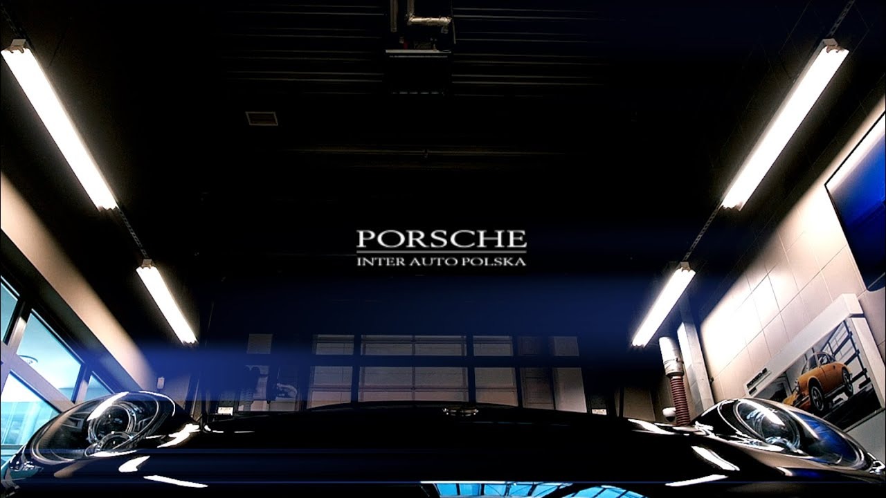 Częściowo widoczny, czarny samochód Porsche w salonie samochodowym, oświetlony jarzeniówkami, z widocznym logo Porsche Inter Auto Polska w tle.