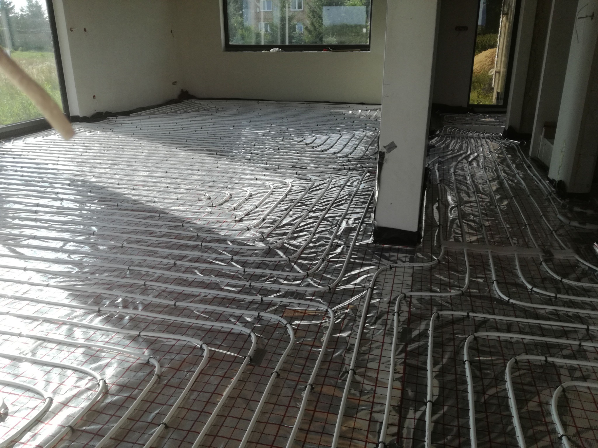 Białe rurki ogrzewania podłogowego rozłożone na folii izolacyjnej w jasnym pomieszczeniu w Lublinie, widok z góry na instalację przed zalaniem wylewką.