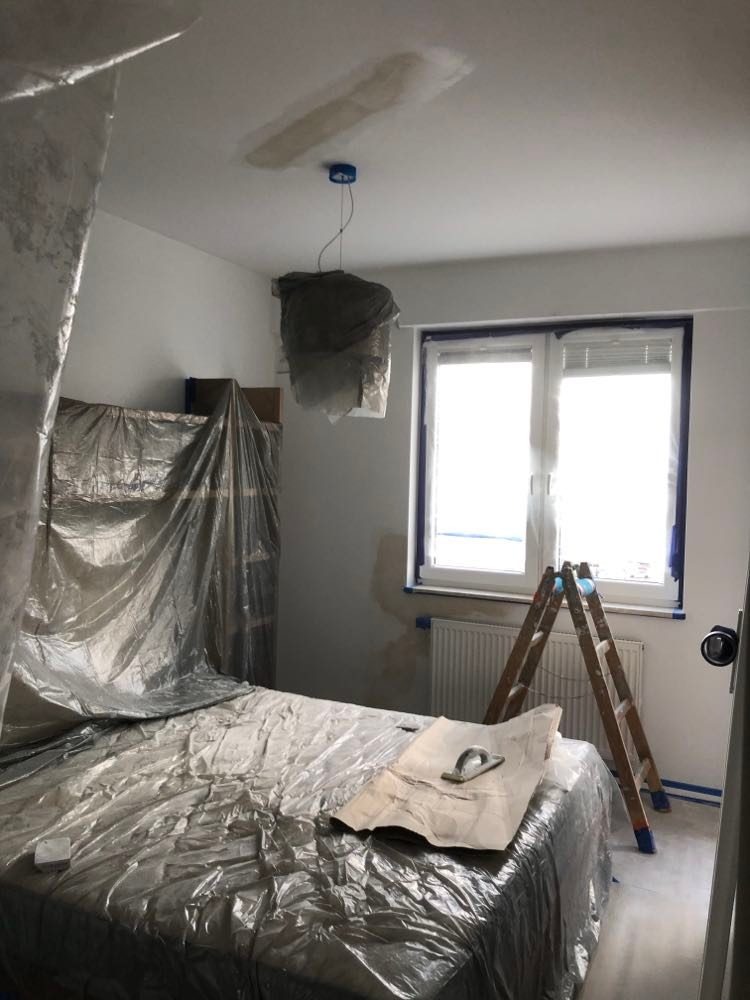 Pokój zabezpieczony folią malarską z widoczną łatą na suficie, drabina oparta o okno, przygotowania do remontu.