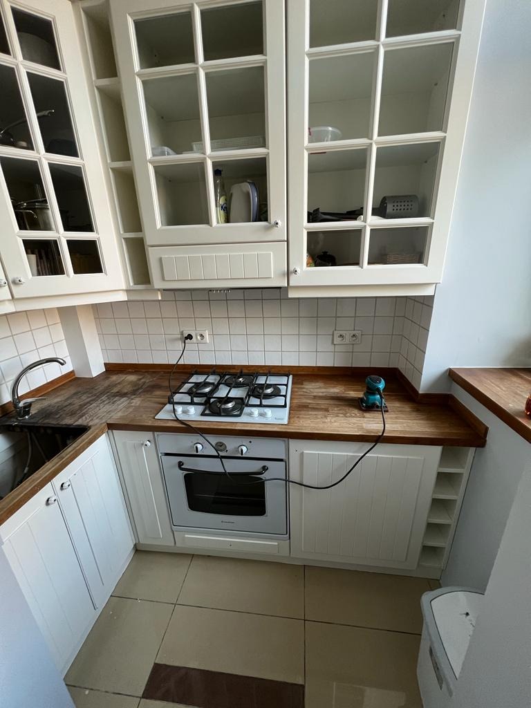 Jasna kuchnia w trakcie prac wykończeniowych: białe szafki z przeszklonymi frontami, drewniany blat, kuchenka gazowa i elektryczna szlifierka na blacie.