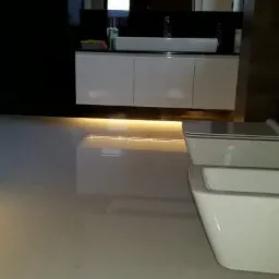 Nowoczesna łazienka z białymi płytkami podłogowymi, podświetlanymi szafkami pod umywalką, toaletą i bidetem z chromowaną armaturą.