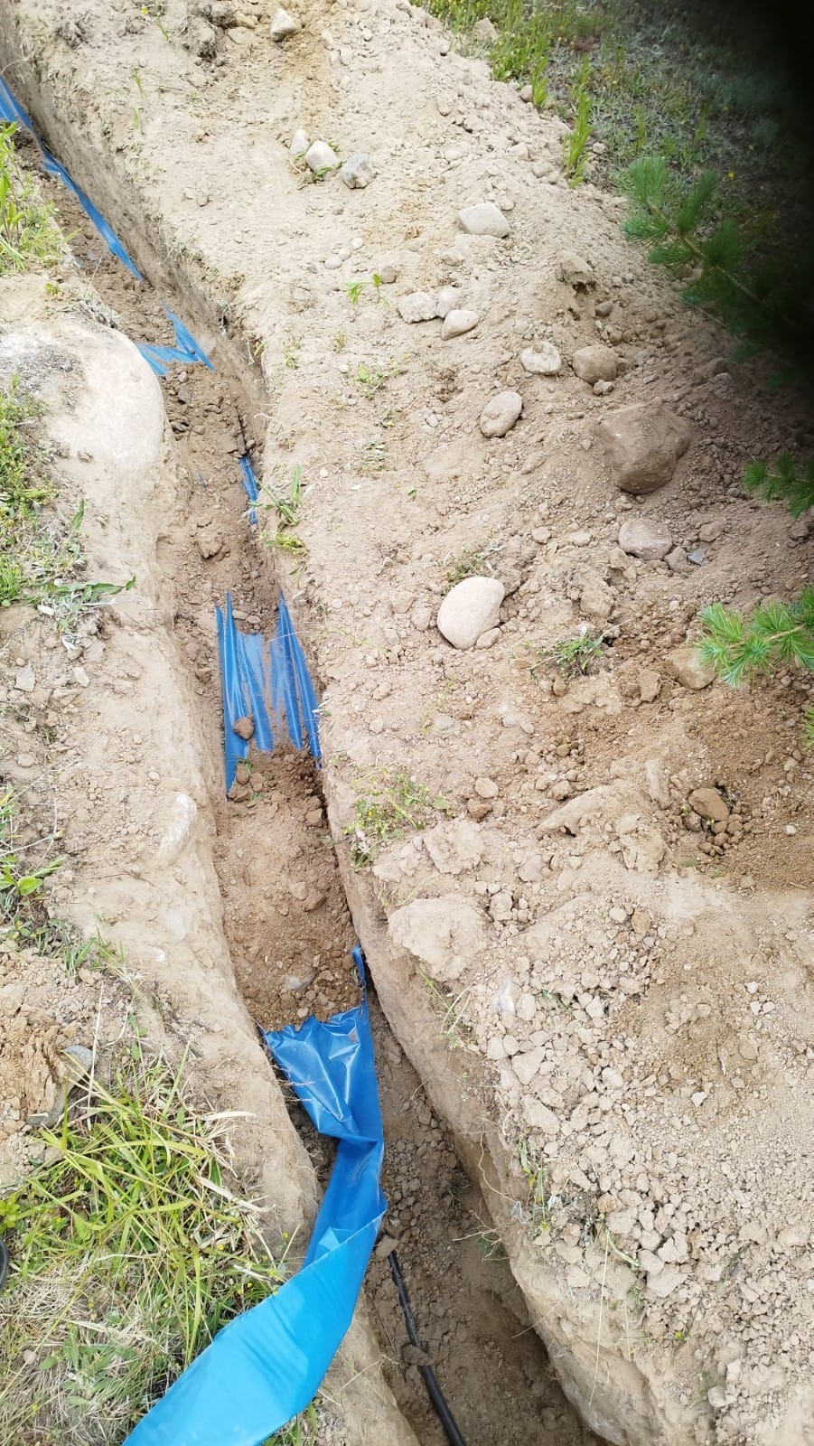 Wykop w ziemi wyłożony niebieską folią, widoczne kable wewnątrz, przygotowanie do zakopania instalacji.
