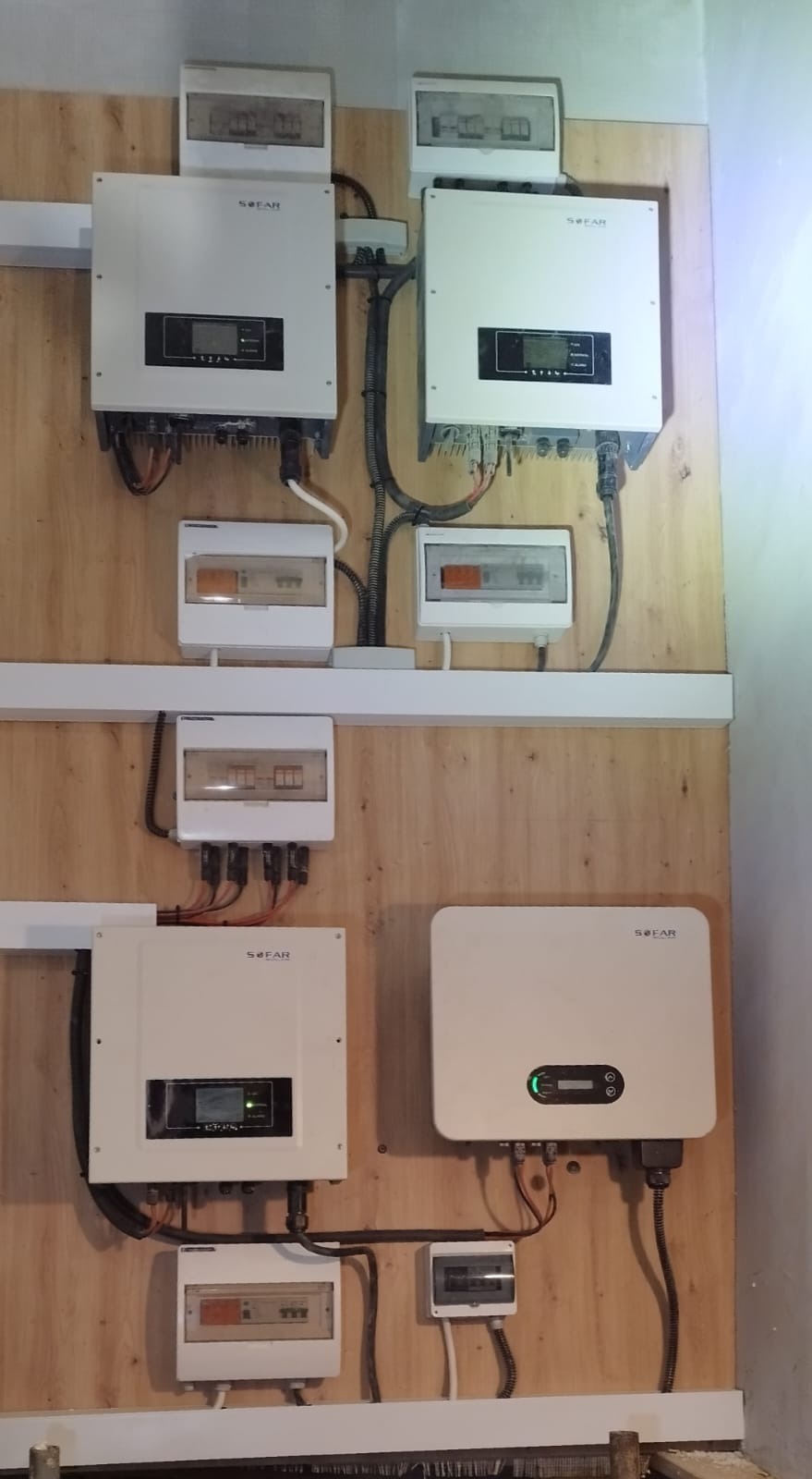 Kompleksowa instalacja fotowoltaiczna z czterema inwerterami SOFAR i rozdzielnicami zamontowana na drewnianej płycie wewnątrz budynku.