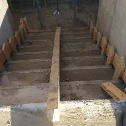 Betonowe schody w trakcie budowy, z widocznym drewnianym szalunkiem, ujęcie z góry, surowe wykończenie.