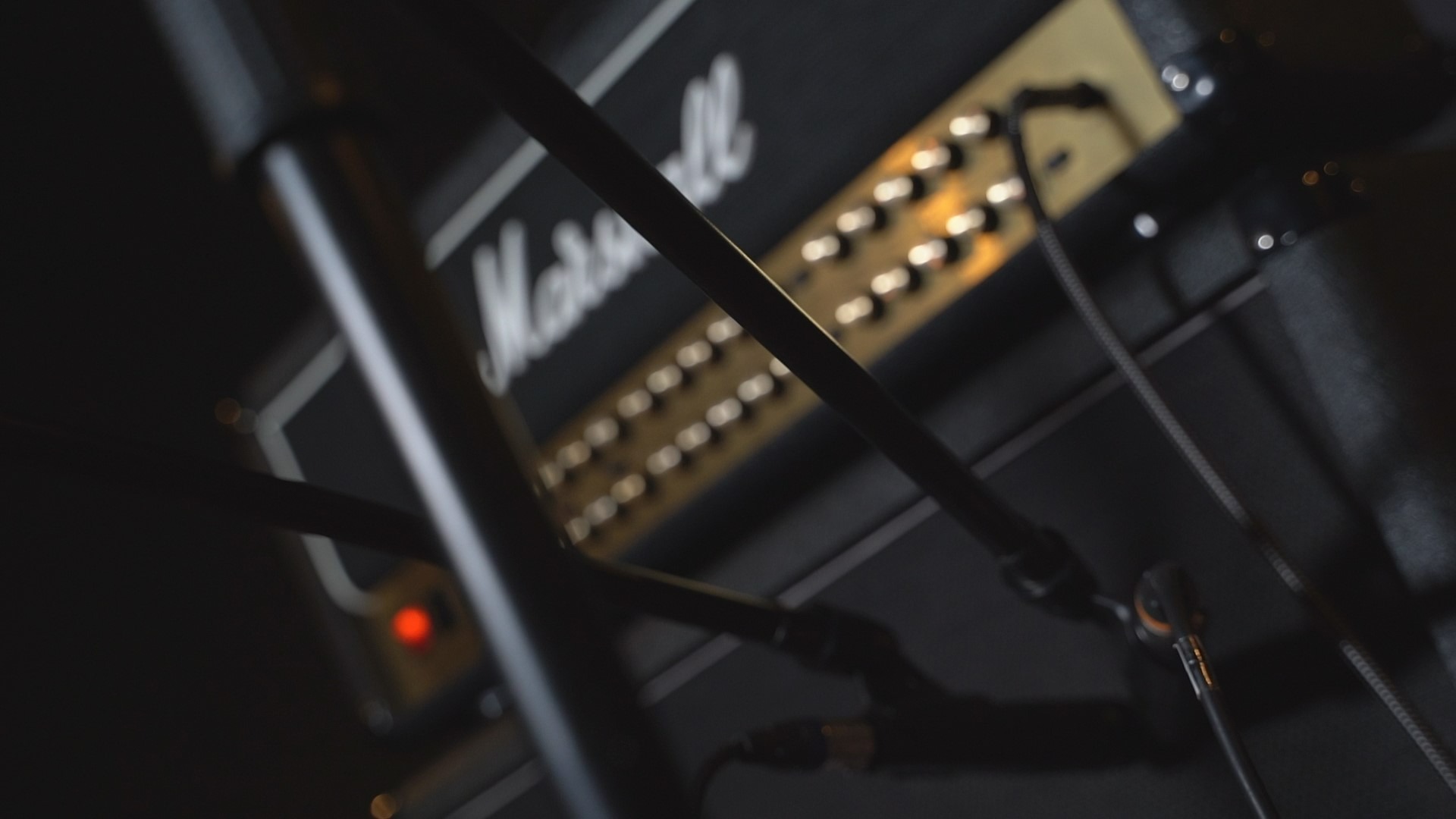 Wzmacniacz gitarowy Marshall z widocznym logiem i potencjometrami, mikrofon na statywie w tle, ujęcie z dołu.