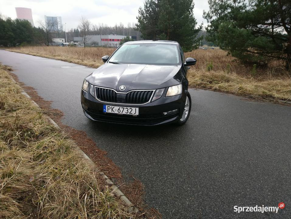 Czarna Skoda Octavia z numerem rejestracyjnym PK 6732J, zaparkowana na mokrej, asfaltowej drodze z widocznym budynkiem w tle.