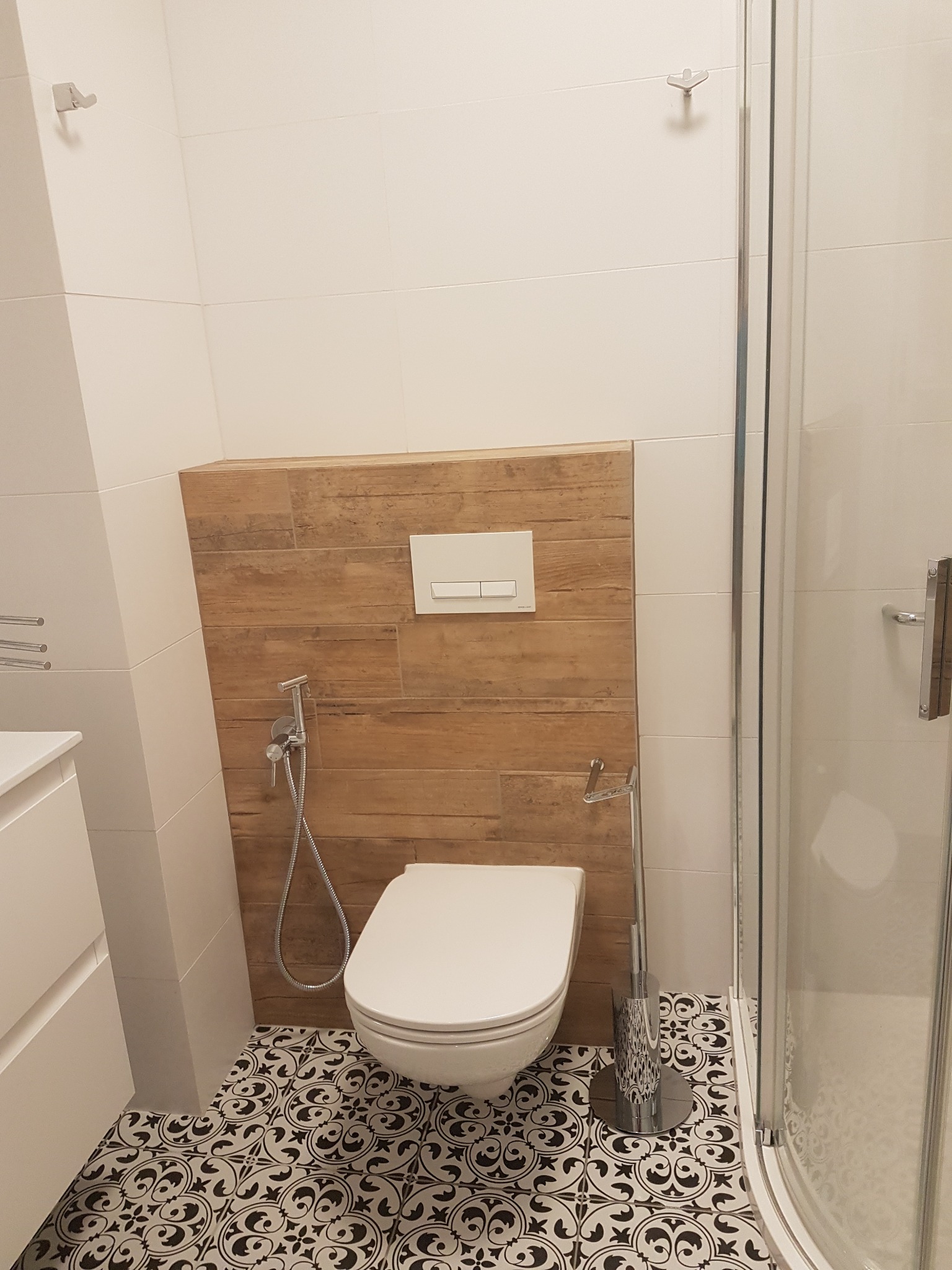 Nowoczesna łazienka z wiszącą toaletą, bidetką, drewnopodobną zabudową stelaża i wzorzystą posadzką w stylu retro.