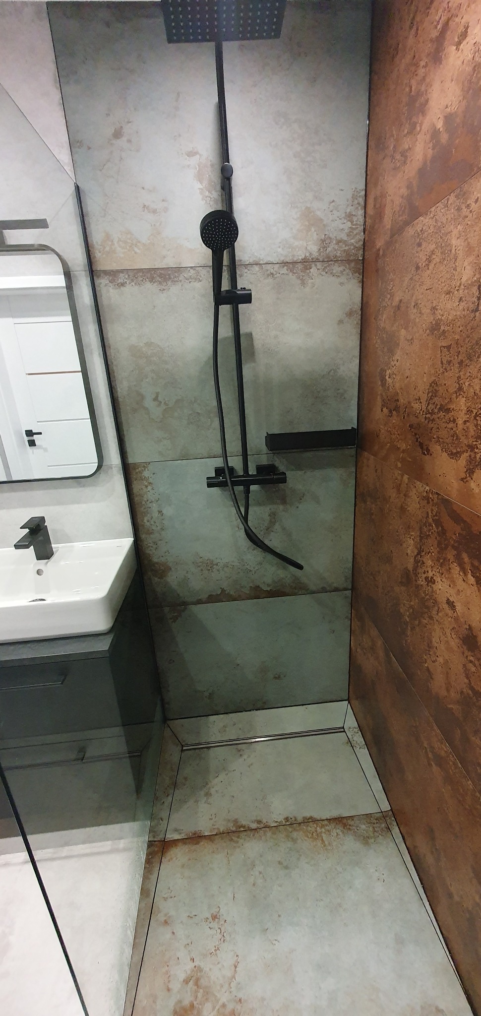 Wykończona łazienka z kabiną prysznicową typu walk-in, czarną armaturą, umywalką nablatową i płytkami imitującymi rdzę na ścianach.