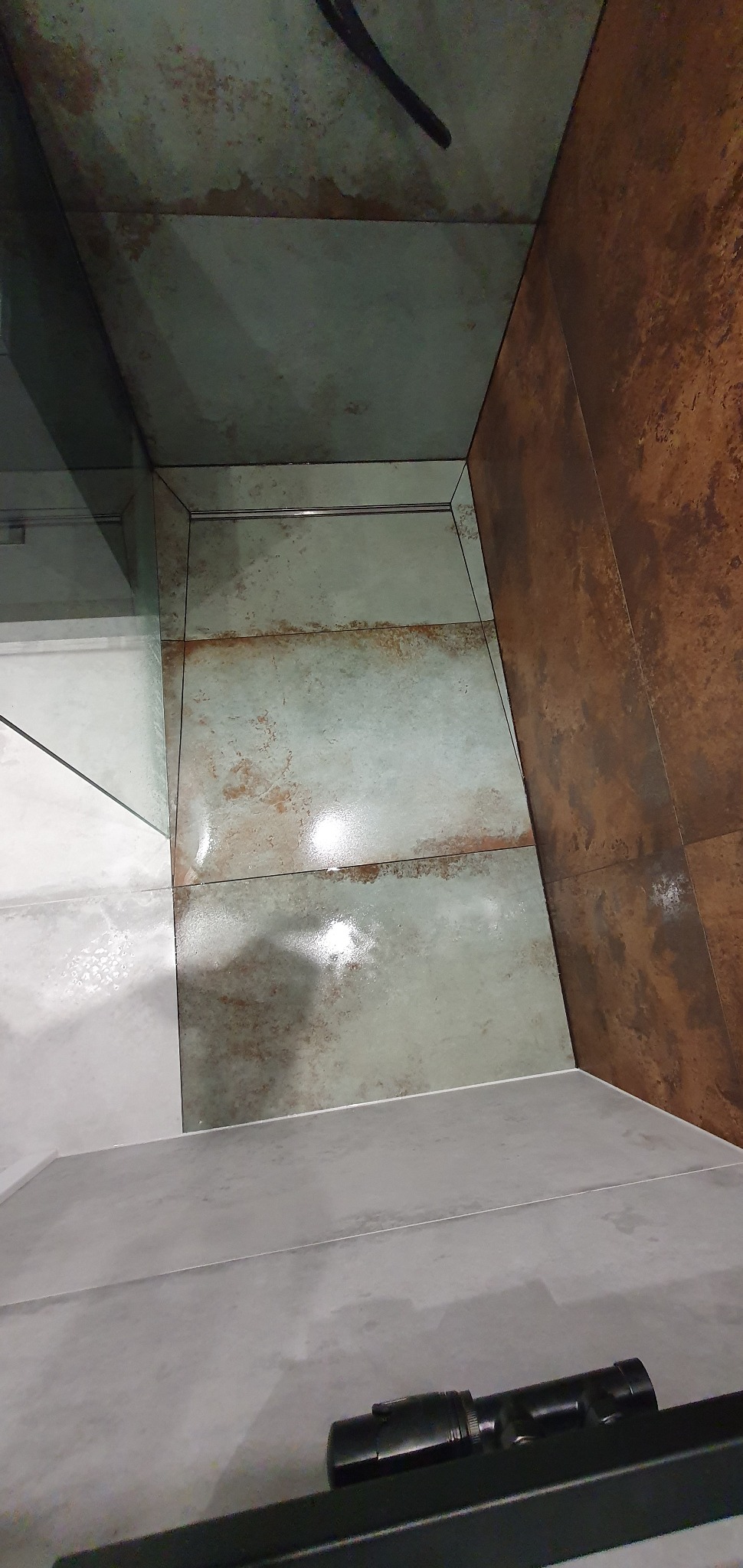 Wykończona kabina prysznicowa z odpływem liniowym i płytkami imitującymi rdzę na ścianach oraz szarą podłogą.