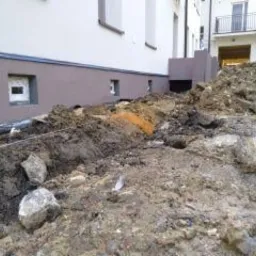 Wykonany wykop pod fundamenty budynku, widoczne ułożone rury drenarskie i wykopana ziemia z kamieniami.