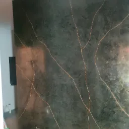 Ściana w pokoju pokryta dekoracyjną, ciemną fakturą z nieregularnymi, złotymi żyłkami, widoczne gniazdka elektryczne i drabina malarska.