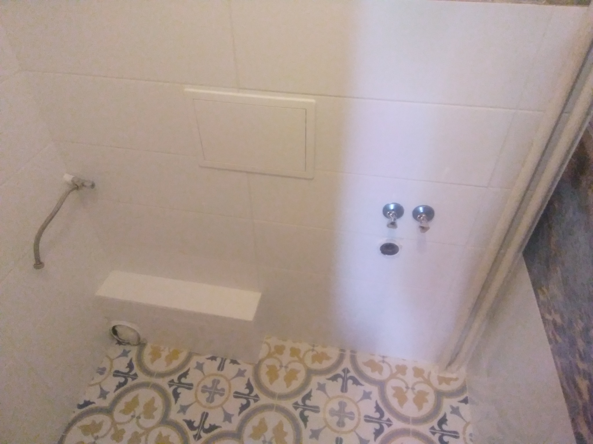 Wykończona łazienka z białą armaturą, ozdobnymi płytkami podłogowymi w stylu retro i ukrytym dostępem rewizyjnym w ścianie.